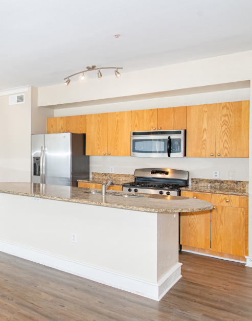 A pristine kitchen featuring stainless steel appliances, stylish wood cabinets, and a sleek bar top counter at MAA Abbey luxury apartments in Dallas, TX