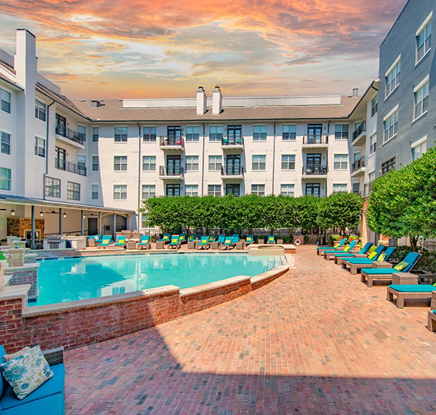 Community poolside area surrounded by lounge chairs with blue cushions and lush greenery situated in the center of the apartment complex at MAA Addison Circle luxury apartments in Addison, TX