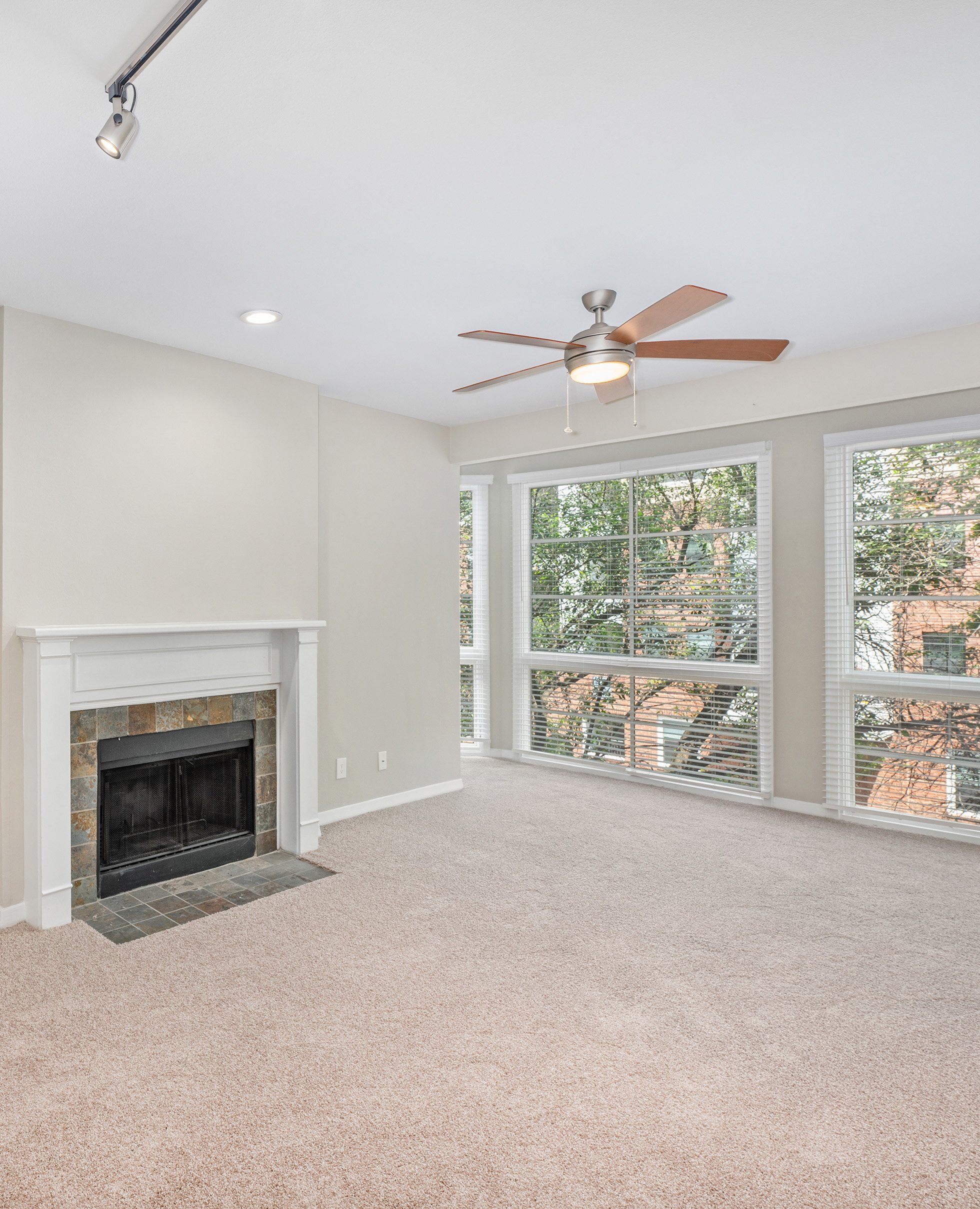 Carpeted empty living room with ceiling fan, picture windows and tiled fireplace at MAA Addison Circle luxury apartments in Addison, TX