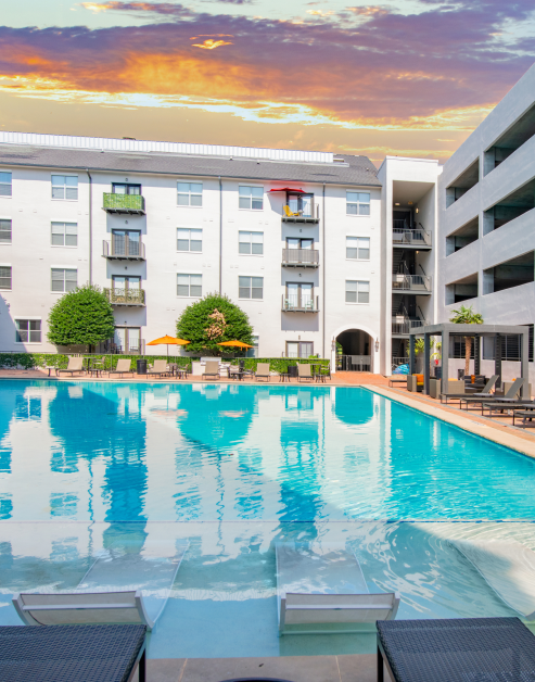 Swimming pool surrounded by lounge chairs with sun umbrellas situated next to the apartment complex at MAA Addison Circle luxury apartments in Addison, TX