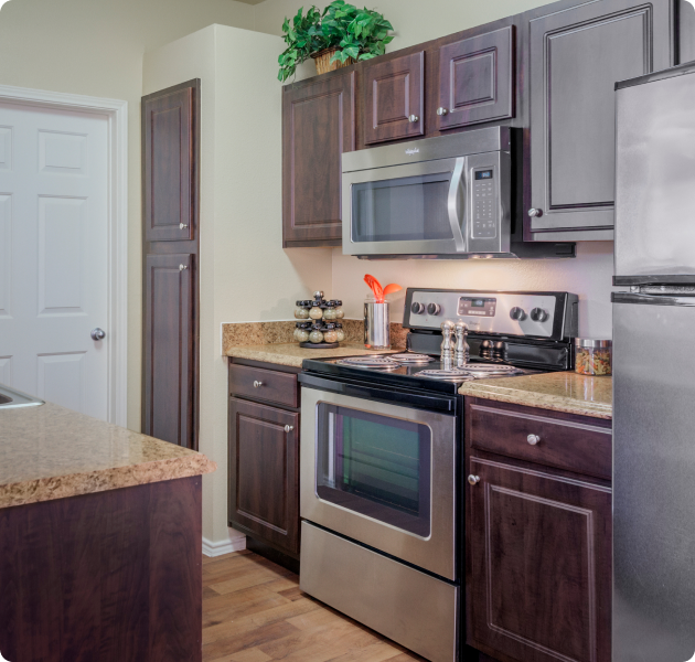 An apartment kitchen with modern stainless steel appliances, dark wood cabinets and granite countertops at MAA Boulder Ridge luxury apartments in Roanoke, TX
