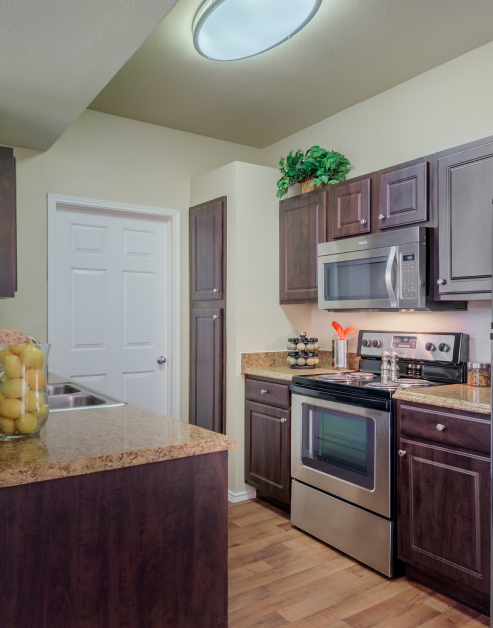 A modern kitchen with stainless steel appliances and dark wood cabinets with granite countertops and hardwood flooring at MAA Boulder Ridge luxury apartments in Roanoke, TX