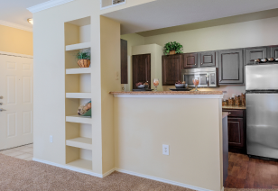 A front view of a kitchen with dark wood cabinets and bar top counter with built-in shelving at MAA Boulder Ridge luxury apartments in Roanoke, TX