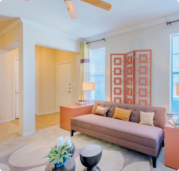 A contemporary-style living room next to an archway entrance doorway, with side light windows and a couch and side tables on carpeted floors at MAA Copper Ridge luxury apartment in Roanoke, TX