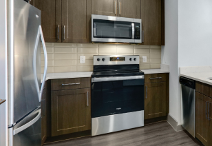 Modern kitchen features dark wood cabinets with white tile backsplash, stainless steel appliances and dark hardwood floors at MAA Copper Ridge luxury apartment in Roanoke, TX