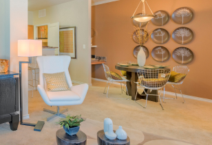 A side view of living room with a white armchair and floor lamp next to a dining area with hanging light fixtures and decorative wall plates with carpeted floors at MAA Copper Ridge luxury apartments in Roanoke, TX