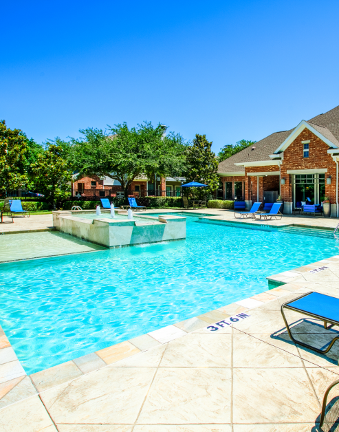 A swimming pool equipped with lounge chairs surrounded by large trees and planters at MAA Copper Ridge luxury apartments in Roanoke, TX