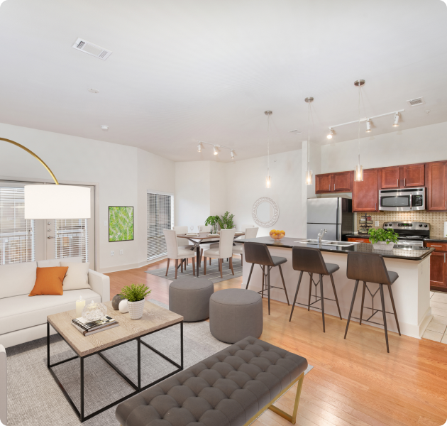 A luxurious living room seating area with modern lighting fixtures next to the kitchen and dining area with hardwood flooring at MAA Eastside luxury apartments in Richardson, TX