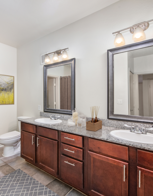 A luxurious bathroom with double vanity sinks and dark wood cabinets with granite countertops and tiled floors at MAA Eastside luxury apartments in Richardson, TX