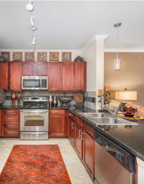 An upscale model kitchen with black granite countertops and wood cabinets, and stainless steel appliances at MAA Eastside luxury apartments in Richardson, TX