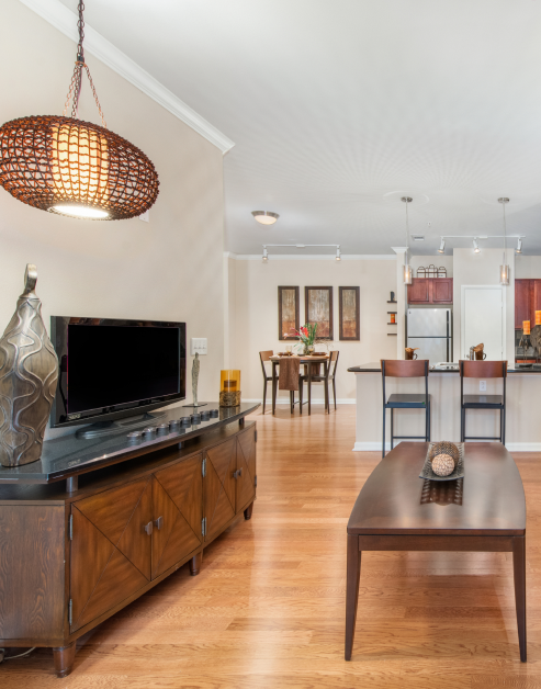 A modern living room with hanging light fixture next to a sleek wooden TV unit and a coffee table near an open dining area at MAA Eastside luxury apartments in Richardson, TX