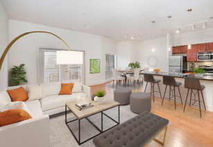 A spacious model living room with sectional sofa and coffee table next to an open kitchen with bar stools and wood flooring at MAA Eastside luxury apartments in Richardson, TX