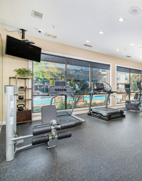 A fitness center featuring treadmills, kettlebells, and a TV with a view of the pool at MAA Fairview luxury apartments in Fairview, TX