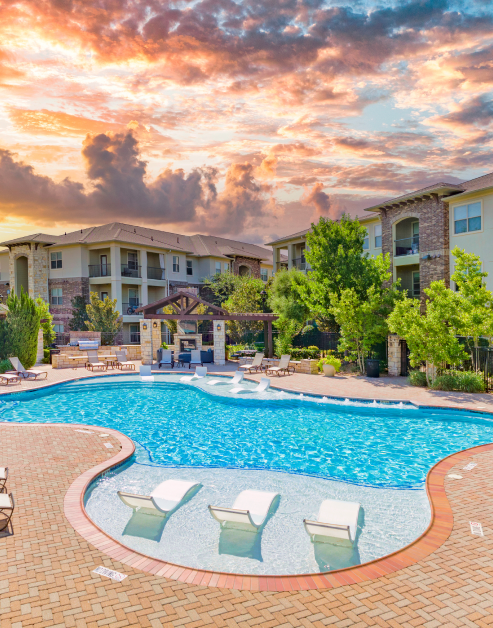 Luxurious swimming pool with a sundeck and lounge chairs, surrounded by trees at MAA Fairview luxury apartments in Fairview, TX
