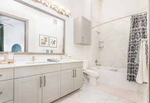 Light-toned bathroom with a large vanity mirror, off-white cabinets and tiled bathtub at MAA Frisco Bridges luxury apartments in Frisco, TX