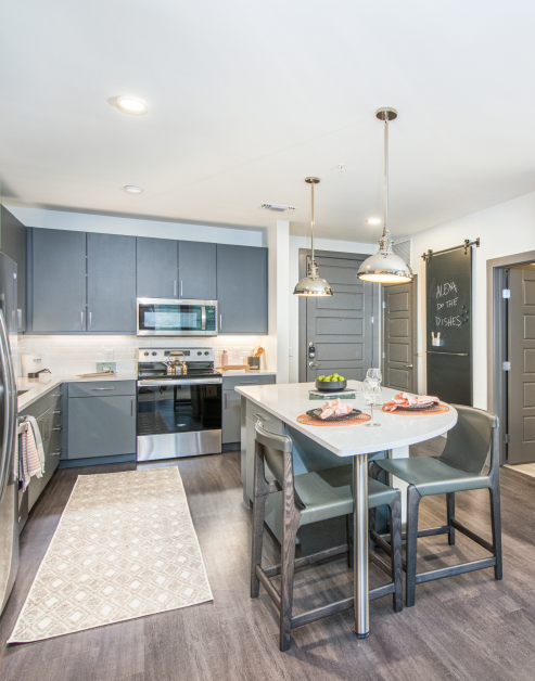 Modern farmhouse style kitchen with gray cabinets, upgraded appliances next to kitchen island with wood floors at MAA Frisco Bridges luxury apartments in Frisco, TX