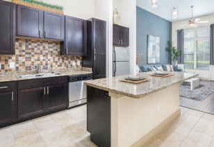 Kitchen with granite countertop island and dark brown cabinets with upgraded appliances at MAA Frisco Bridges luxury apartments in Frisco, TX