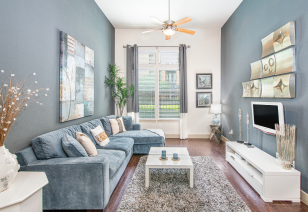 Side view of living room with a ceiling fan, TV above entertainment center and a blue fabric couch at MAA Frisco Bridges luxury apartments in Frisco, TX