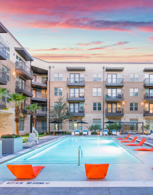 Resort-style swimming pool and sundeck surrounded by lounge chairs with palm trees at MAA Frisco Bridges luxury apartments in Frisco, TX