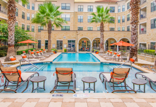 Wide view of swimming pool and sundeck with lounge chairs surrounded by trees, situated in the center of the apartment complex at MAA Frisco Bridges luxury apartments in Frisco, TX