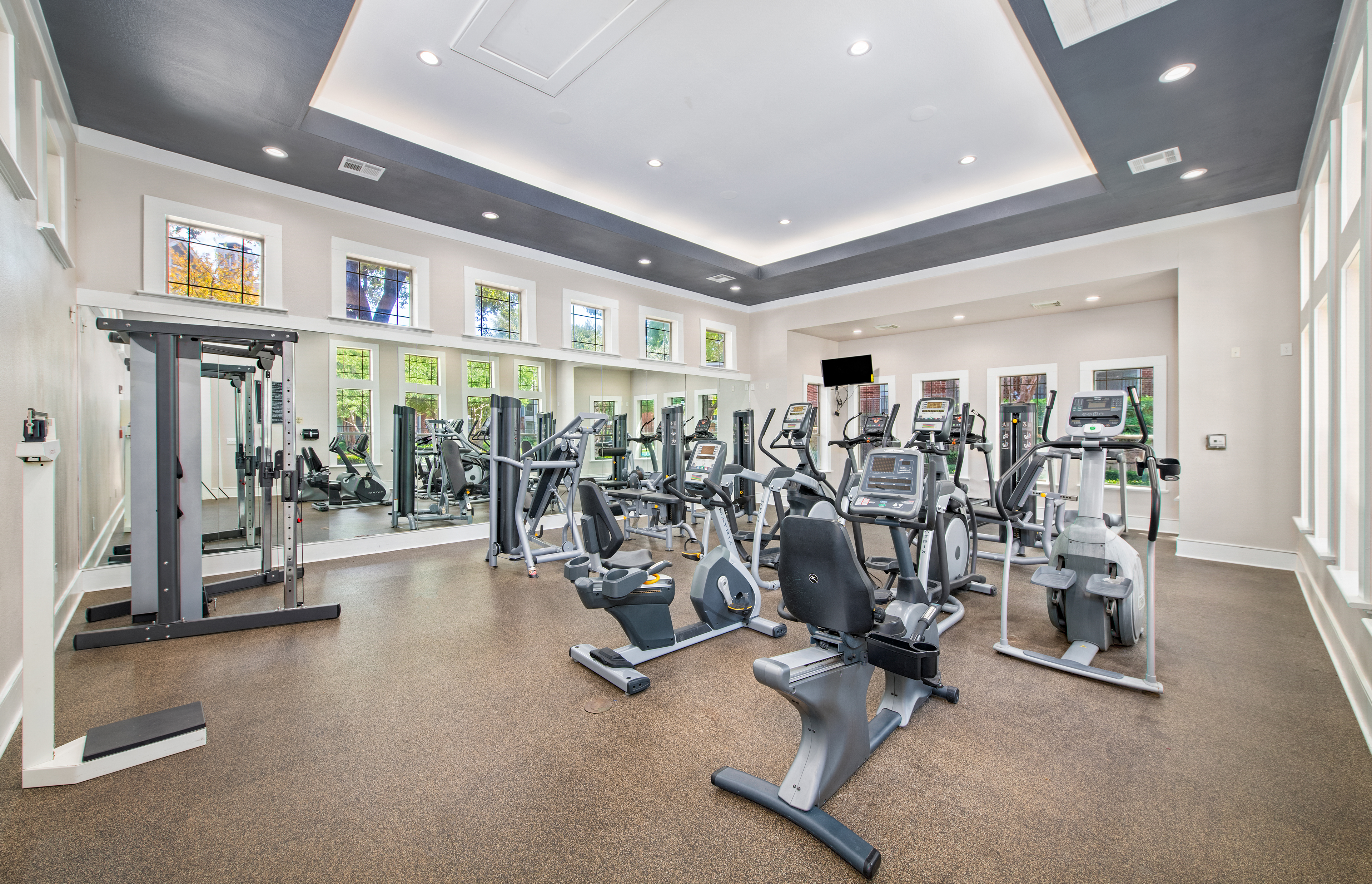 State-of-the-art fitness center with recessed lighting and large windows with a variety of weight machines at MAA Grand Courtyards luxury apartments in Grand Prairie, TX