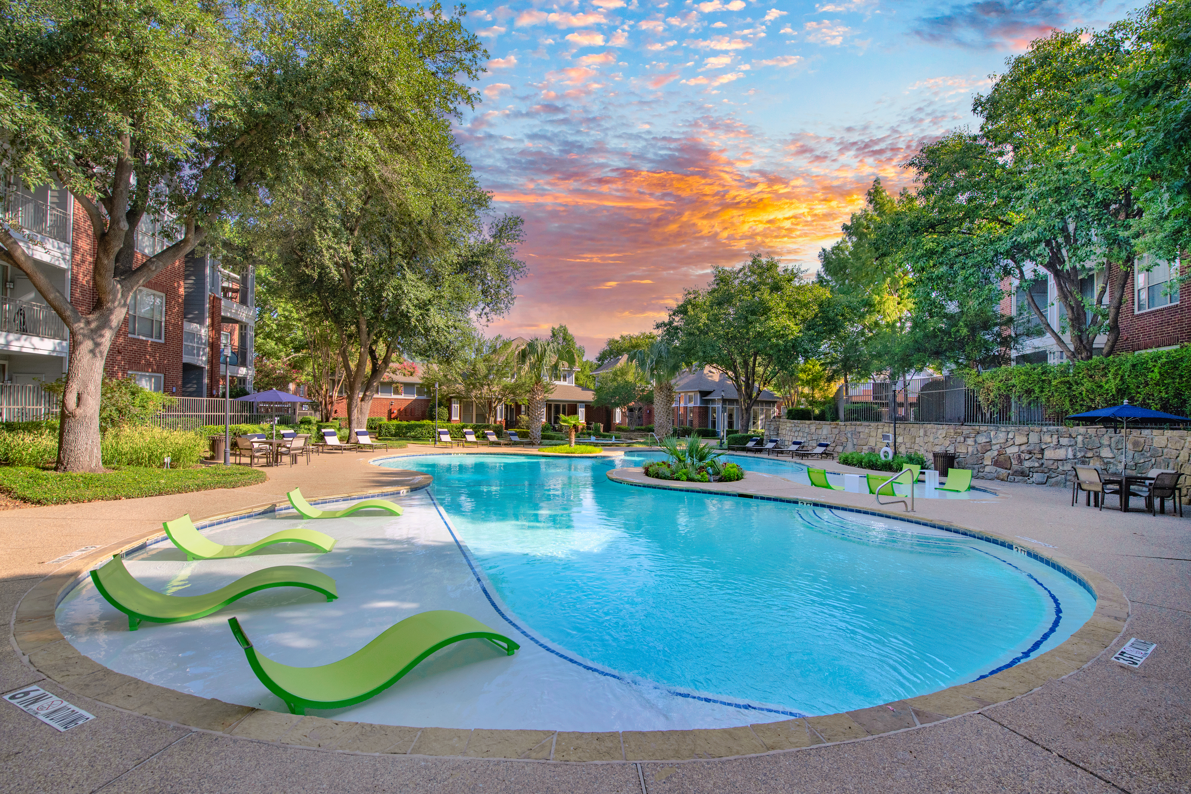 A side view of the swimming pool with green sundeck chairs surrounded by trees and plants at MAA Grand Courtyards luxury apartments in Grand Prairie, TX