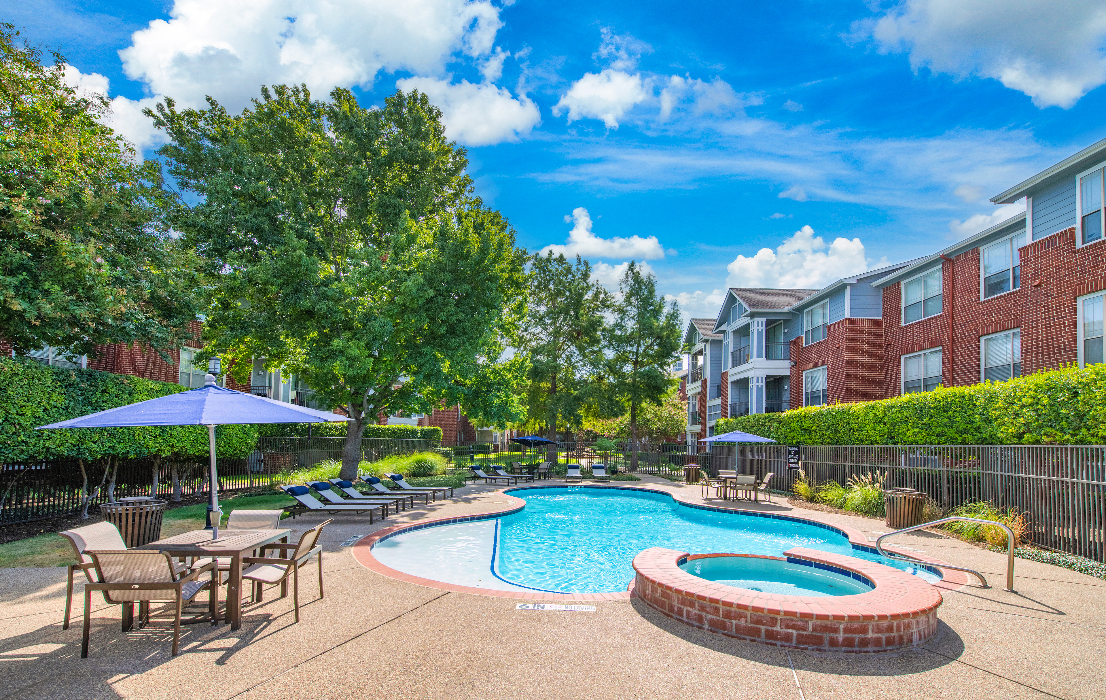 A second pool in the center of apartment complex surrounded by trees and lounge chairs with a hot tub and a patio table with chairs at MAA Grand Courtyards luxury apartments in Grand Prairie, TX