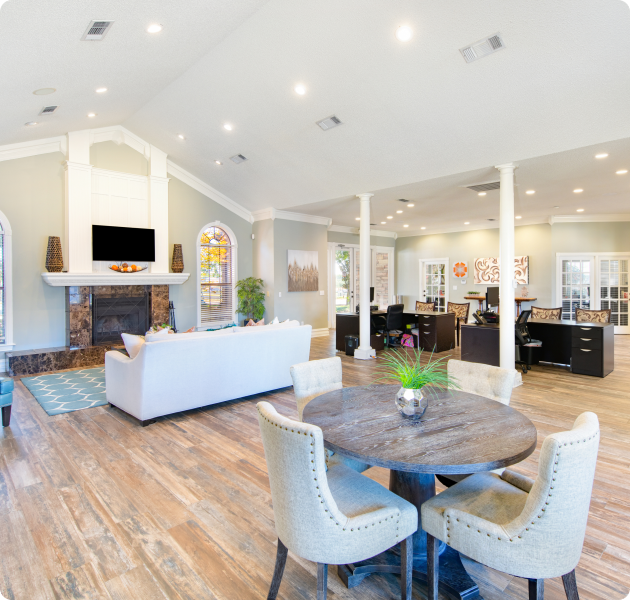 Community clubhouse with multiple lounge and sitting areas with a wall-mounted TV above a marble fireplace and a couch, next to leasing office area at MAA Grapevine luxury apartments in Grapevine, TX