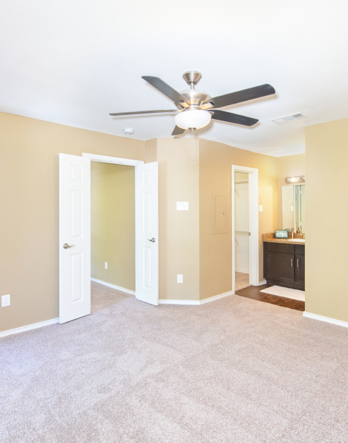A open-space empty master bedroom with a double-door entrance and vanity mirror with cabinets outside of bathroom at MAA Grapevine luxury apartments in Grapevine, TX