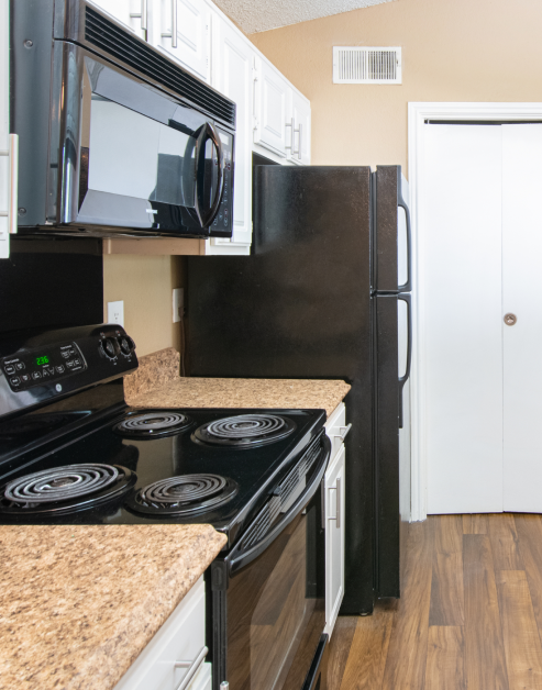 An upscale kitchen features modern black appliances and white cabinets and tan countertops with dark wood flooring at MAA Grapevine luxury apartments in Grapevine, TX