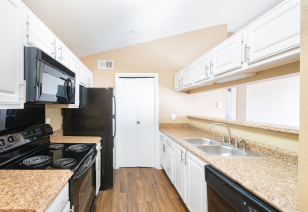 Side kitchen view of bar top counter with white overhead cabinets, upgraded appliances and wood floors at MAA Grapevine luxury apartments in Grapevine, TX