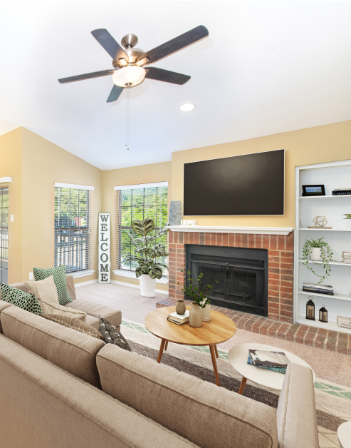 A spacious living room with natural light and vaulted ceilings with recessed lighting, a wall-mounted TV above a brick fireplace next to couch with a coffee table at MAA Grapevine luxury apartments in Grapevine, TX