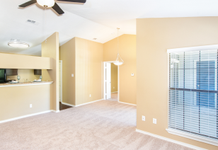 A side view of an open-space empty living room with vaulted ceilings and recessed lights with carpeted floors next to the kitchen at MAA Grapevine luxury apartments in Grapevine, TX