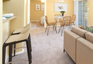 A furnished living room area next to a dining area and large windows, and bar top stools across from a couch, with a doorway to bedroom at MAA Grapevine luxury apartments in Grapevine, TX