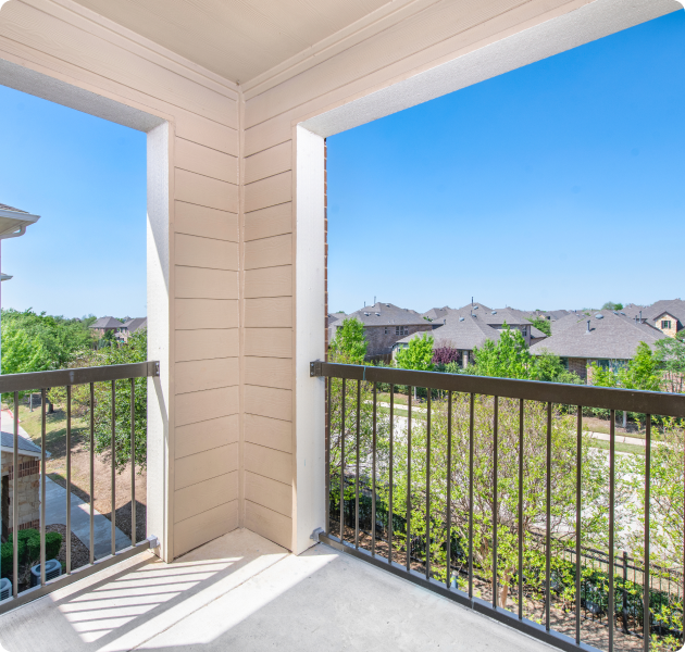 A balcony view from an apartment overlooking a neighborhood rooftops with trees at MAA Hebron luxury apartments in Carrollton, TX