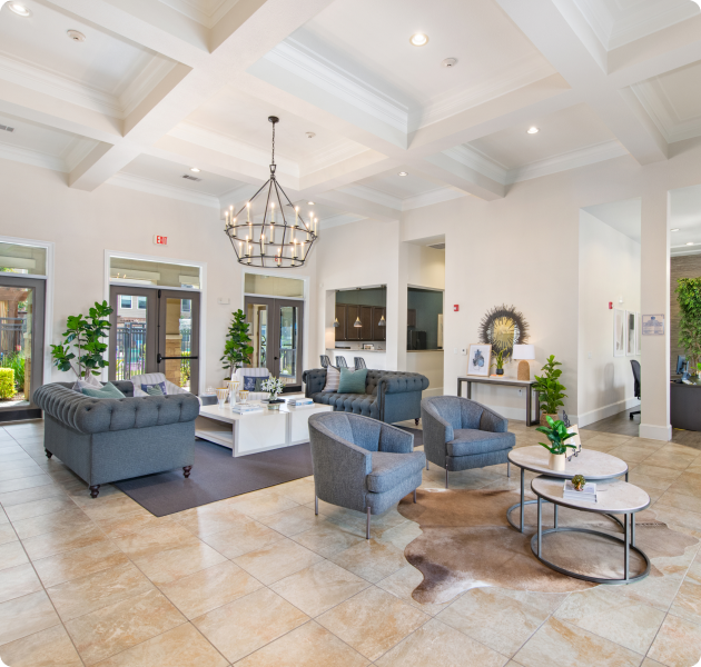 A luxurious community lounge with a chandelier features multiple seating areas with sofa set and armchairs and tiled flooring at MAA Hebron luxury apartments in Carrollton, TX