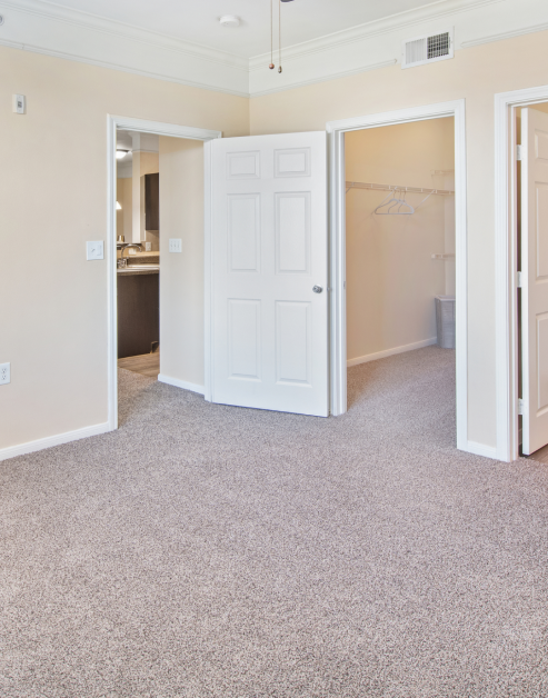 Spacious master bedroom with carpeted floors with two open doorways to an ensuite bathroom and a walk-in closet at MAA Hebron luxury apartments in Carrollton, TX
