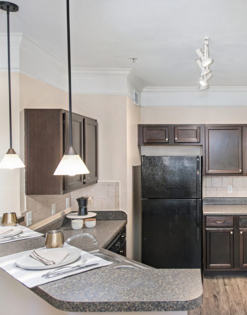 An upscale kitchen with hanging light fixtures, dark wooden cabinets with granite countertops and hardwood flooring at MAA Hebron luxury apartments in Carrollton, TX
