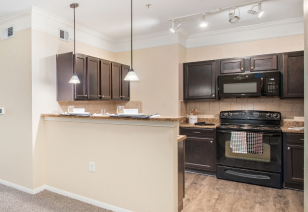 A luxurious kitchen with hanging light fixtures, granite countertops with dark cabinets, modern appliances and hardwood floors at MAA Hebron luxury apartments in Carrollton, TX