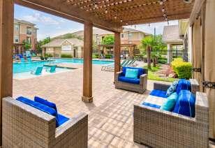 Poolside seating area under a wooden pergola, featuring a wicker furniture set and lounge chairs at MAA Hebron luxury apartments in Carrollton, TX