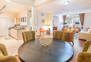 A contemporary kitchen adjacent to a dining space with a dark round table and suede chairs, next to living area at MAA Heights luxury apartments in Dallas, TX