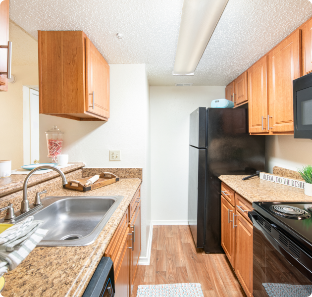 A modern kitchen with wooden cabinets, granite countertops, stainless steel sink, and black appliances at MAA Highlands North luxury apartments in Dallas, TX