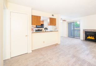 An open-space living room with carpeted floors and a fireplace, adjacent to the kitchen at MAA Highlands North luxury apartments in Dallas, TX