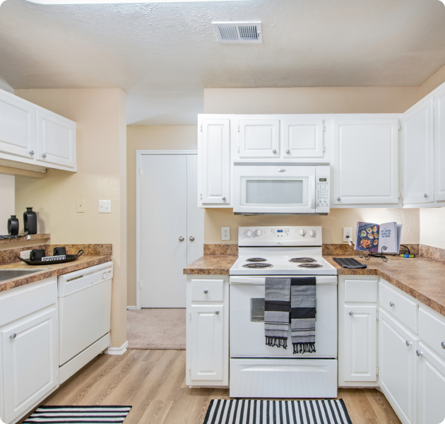 A modern kitchen features white cabinets, a stove, a microwave, a dishwasher and wood floors at MAA Highwood luxury apartments in Plano, TX