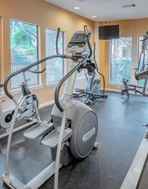 A fitness center space showcasing elliptical machines alongside a wall-mounted TV at MAA Highwood luxury apartments in Plano, TX