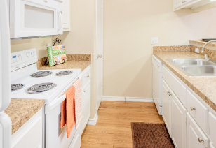 A modern kitchen featuring white cabinets, wood flooring, and a sleek white stove and microwave at MAA Highwood luxury apartments in Plano, TX