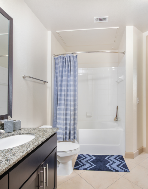 Modern bathroom with marbled countertop, dark brown cabinets and large wood-framed vanity mirror next to bathtub with tiled flooring at MAA Katy Trail luxury apartments in Dallas, TX