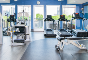 A fitness room featuring treadmills, ellipticals, an exercise bench next to large picture windows at MAA Katy Trail luxury apartments in Dallas, TX