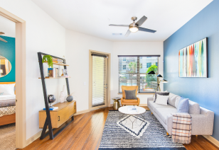 A side view of living room with a white couch and coffee table, ceiling fan next to large windows with wood flooring at MAA Katy Trail luxury apartments in Dallas, TX