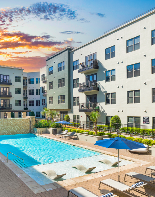 A swimming pool with sun deck, surrounded by lounge chairs, trees and plants at MAA Katy Trail luxury apartments in Dallas, TX